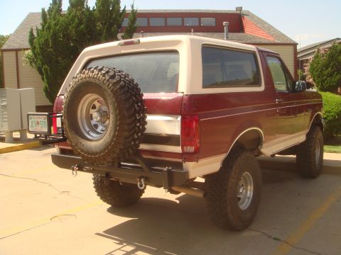 1992 Ford Bronco - Lifted two-tone maroon and tan Ford Bronco shot from the rear three-quarter in a parking lot, fitted with a custom black tubular rear bumpe…