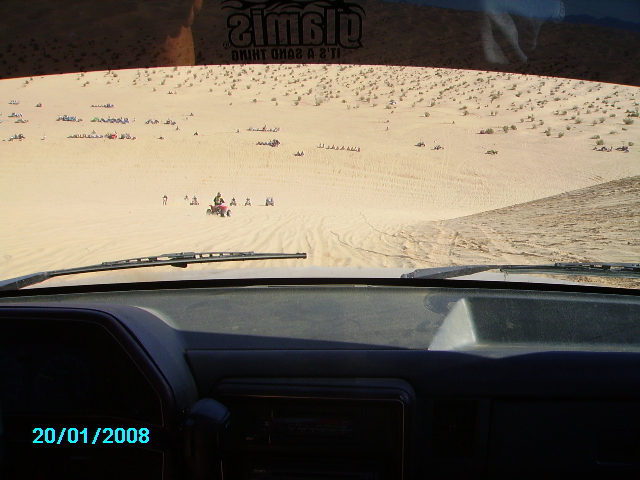 Interior view of a vehicle in sand dunes with ATVs and other vehicles visible