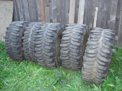 1993 Ford Bronco - Four chunky off-road tires are shown leaning against a weathered wooden fence outdoors.