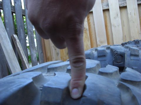 1993 Ford Bronco - A finger presses into the aggressive tread pattern of an off-road tire, with a wooden fence visible behind.