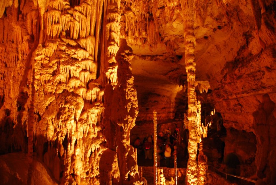 Cave interior with numerous stalactites and stalagmites illuminated in orange light