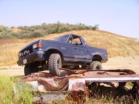 1990 Ford Bronco - This Ford Bronco is positioned over a derelict vehicle in a dry, grassy field.