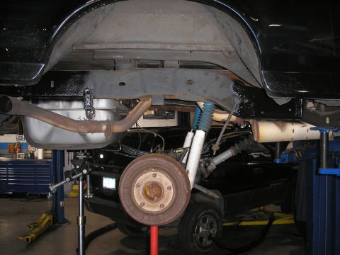 1995 Ford Bronco - The rear suspension and exhaust system of a black vehicle are visible while it is raised on a lift in a garage.