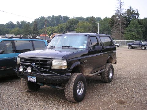 1995 Ford Bronco - A black Ford Bronco is parked on a gravel lot next to a blue van.
