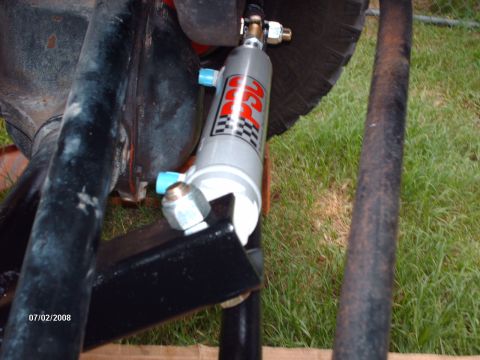 1982 Ford F-100 - Close-up of a steering stabilizer with a checkered logo, attached to vehicle suspension components.