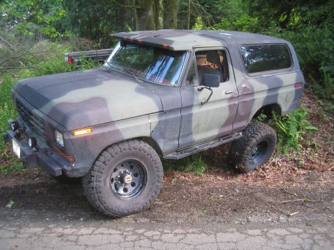 1979 Ford Bronco - This lifted 1978 Ford Bronco is painted in a camouflage pattern and sits on a dirt road surrounded by trees.