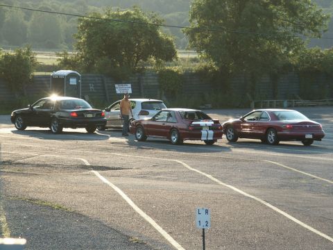 2001 Mercury Grand Marquis - Cars gathered in a parking lot, with a portable toilet and signage in the background.