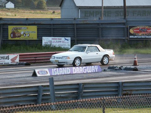2001 Mercury Grand Marquis - A white convertible cruises down the drag strip at Island Dragway, with various advertisements visible in the background.