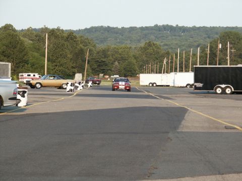 2001 Mercury Grand Marquis - A car with red and white stripes drives down a track with trailers and trees in the background.