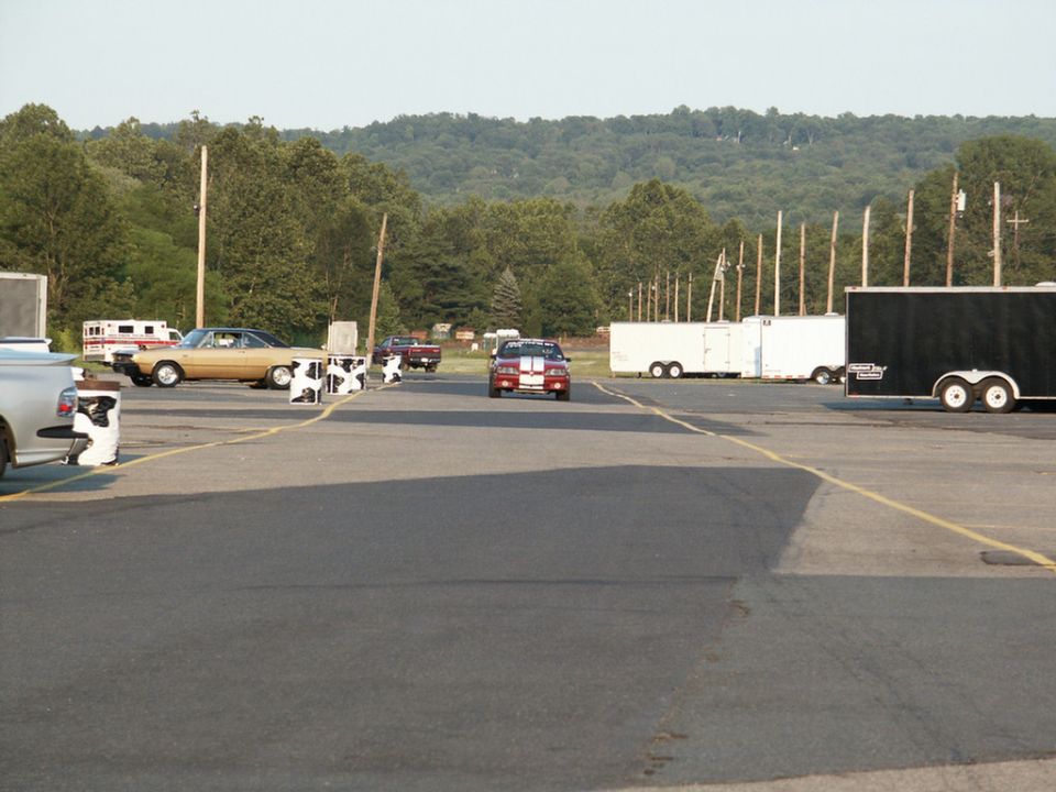 Red and white striped car driving on asphalt, trailers parked nearby
