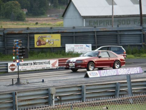 2001 Mercury Grand Marquis - A red Ford Mustang is lined up at Island Dragway, with a dark SUV visible behind it.