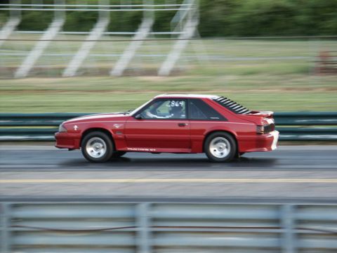 2001 Mercury Grand Marquis - A red coupe with louvers on the rear window is captured in motion on a race track.