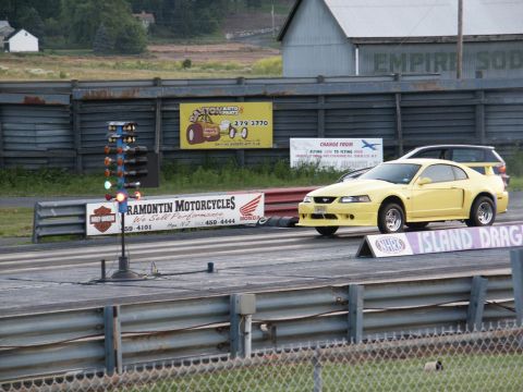2001 Mercury Grand Marquis - A yellow Ford Mustang is staged at the starting line of a drag strip, with a Christmas tree light system ready for the race.