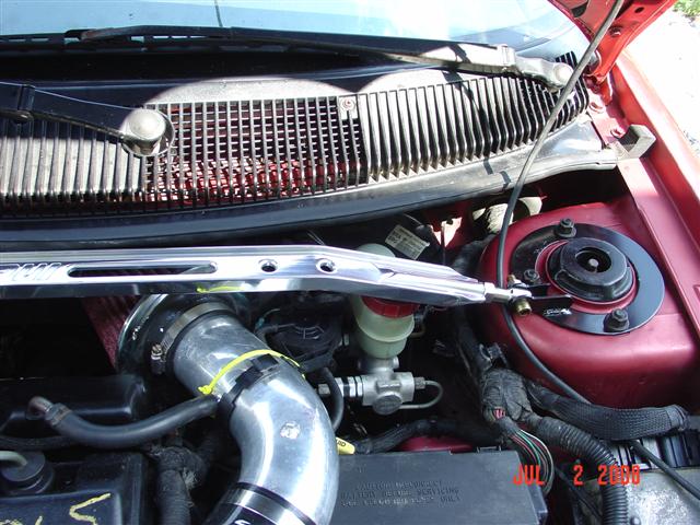 Red engine bay with chrome strut bar, silver intake pipe, and visible brake fluid reservoir
