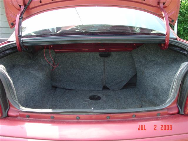 Red car trunk interior with gray carpet lining and visible wiring