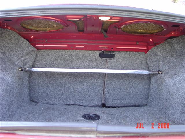 Red car trunk interior with grey carpet and a silver strut bar. Date stamp reads JUL 2 2006