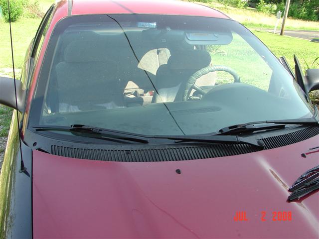 Red car interior showing dashboard, steering wheel, and seats through the windshield. Hood is visible in foreground