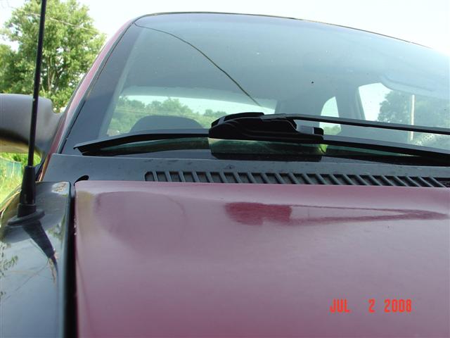 Maroon car hood and black fender with antenna, close-up on windshield wiper