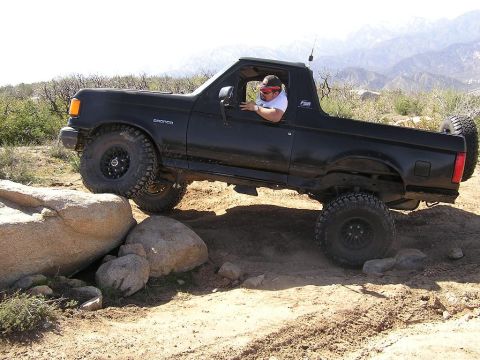 1990 Ford Bronco - A black Ford Bronco navigates a rocky trail with a driver behind the wheel.