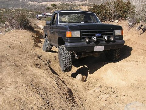 1990 Ford Bronco - A black Ford Bronco navigates a steep dirt path in a dry, hilly landscape.