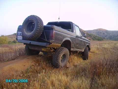1990 Ford Bronco - This black Ford Bronco is shown from the rear, lifted and equipped for off-road use on a dirt path.