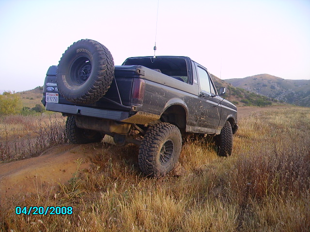 Black Ford Bronco with spare tire on rear, lifted suspension, off-road tires, driving on dirt path