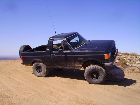 1990 Ford Bronco - This black 1990 Ford Bronco is captured in a three-quarter front view while navigating a rocky, dirt terrain.