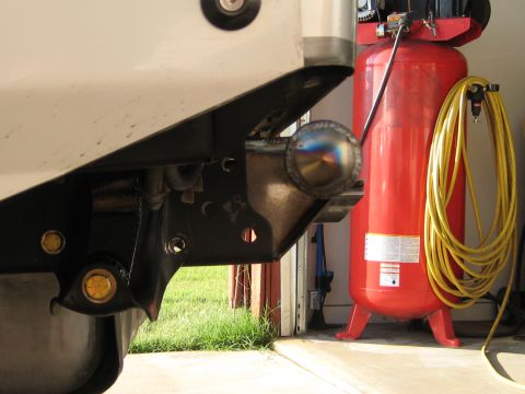 1996 Ford Bronco - A close-up view of a rear bumper hitch assembly, with a red air compressor and coiled yellow hose visible in the background.