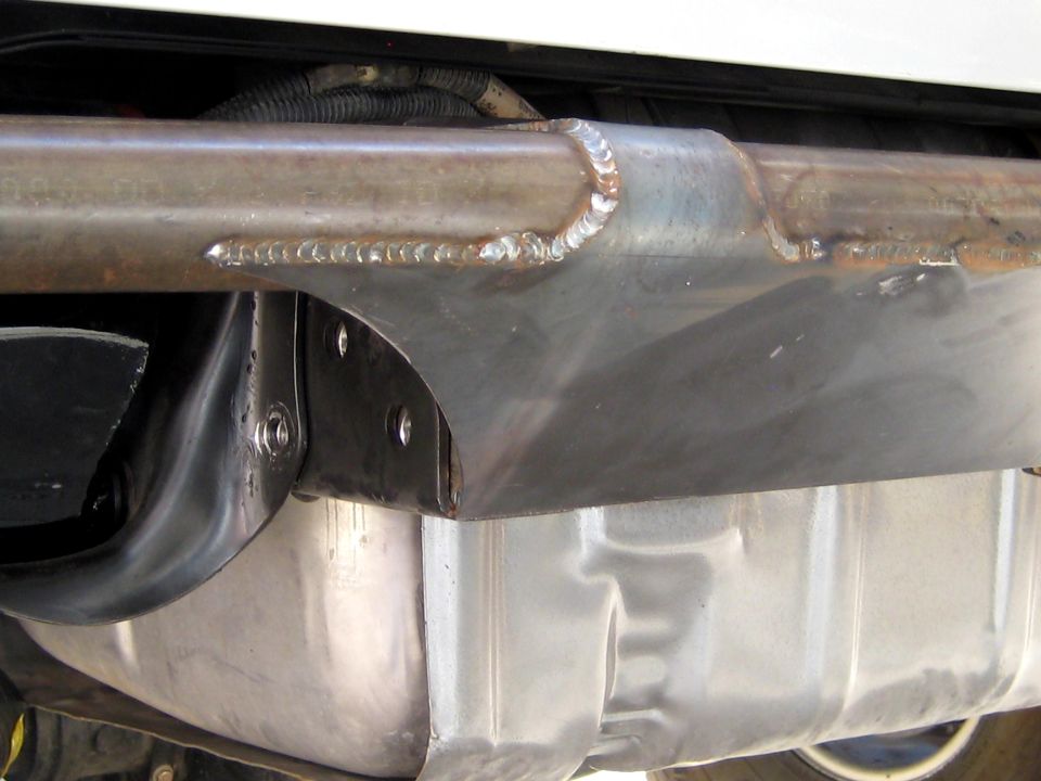 Close-up of a custom metal bracket welded to a vehicle frame, above a silver fuel tank