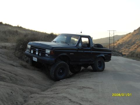 1990 Ford Bronco - This 1990 Ford Bronco is shown off-roading on a dusty trail with hills in the background.