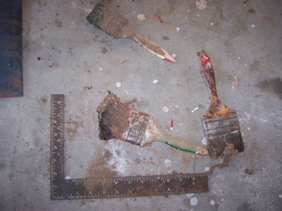 Three dirty paint brushes and a metal ruler on a concrete floor
