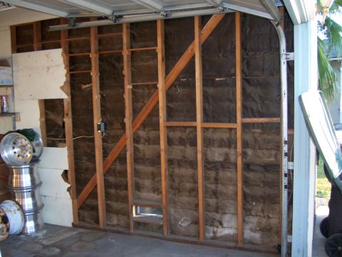1991 Ford Bronco - Stacked aluminum wheels sit near a garage wall with exposed studs and insulation.