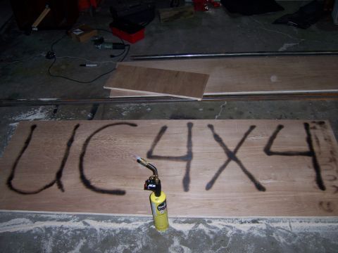 1991 Ford Bronco - A propane torch is positioned over a plywood sheet with "UC 4X4" spray-painted on it.