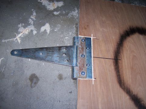 1991 Ford Bronco - A metal T-hinge is attached to a piece of plywood, resting on a concrete surface.