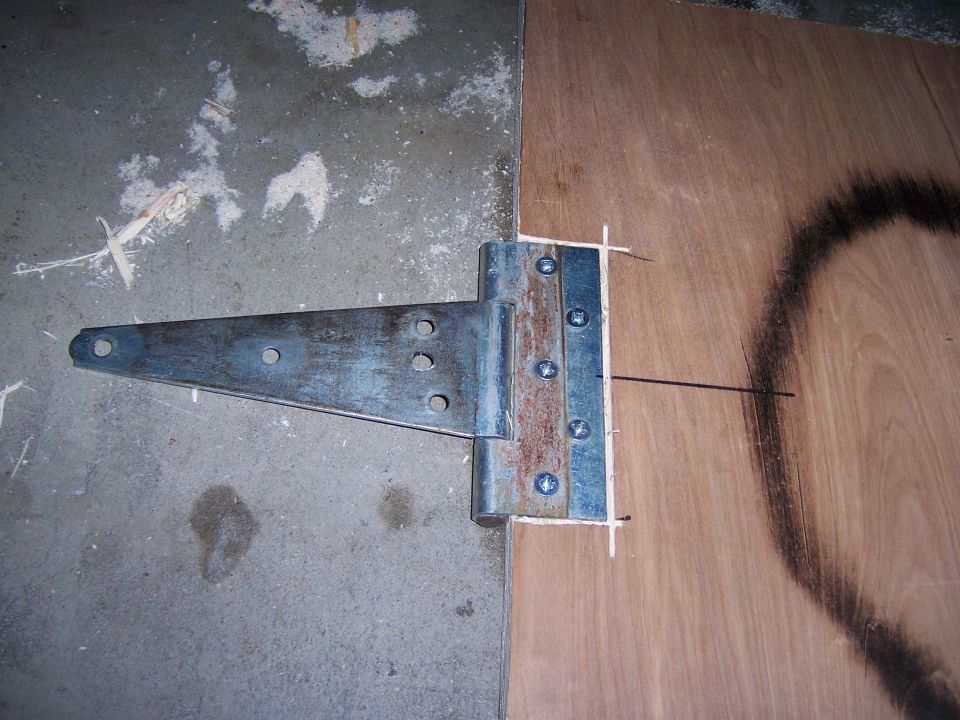 Metal T-hinge attached to plywood with screws, on concrete floor
