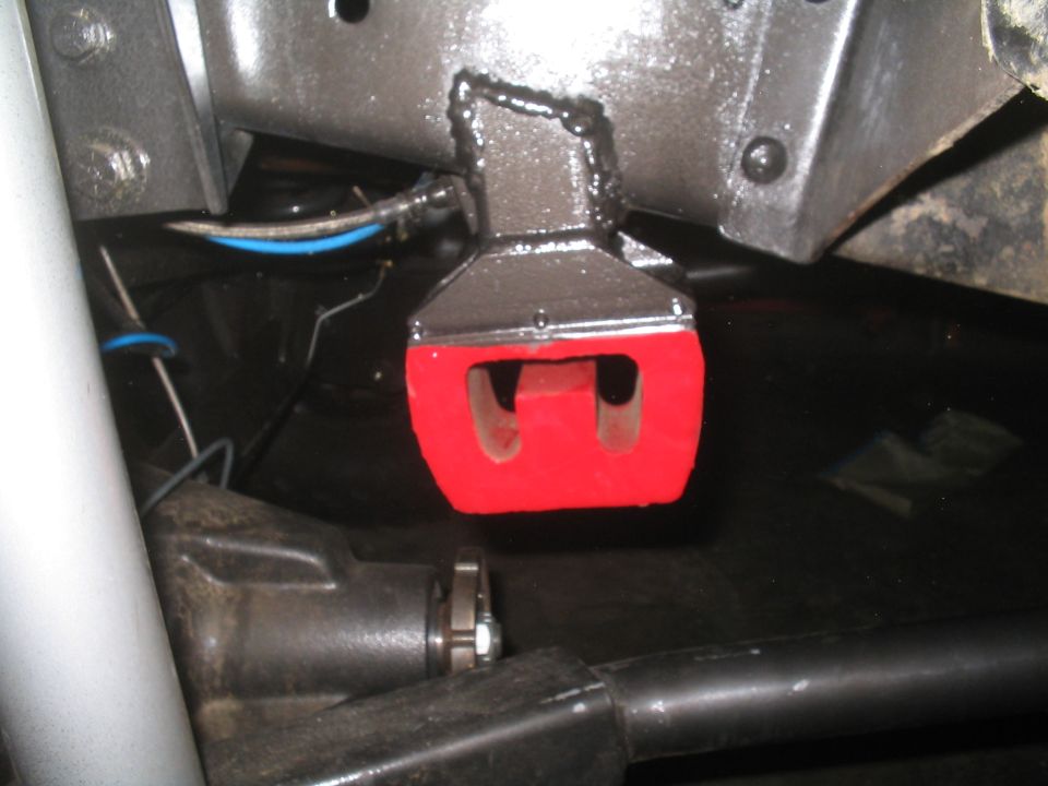 Close-up of a red suspension bushing attached to a metal bracket with visible welds