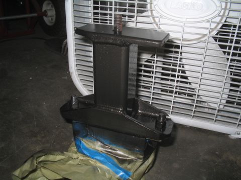1979 Ford Bronco - A black metal bracket with bolts and a threaded rod is shown in front of a white box fan, with blue tape and brown paper underneath.