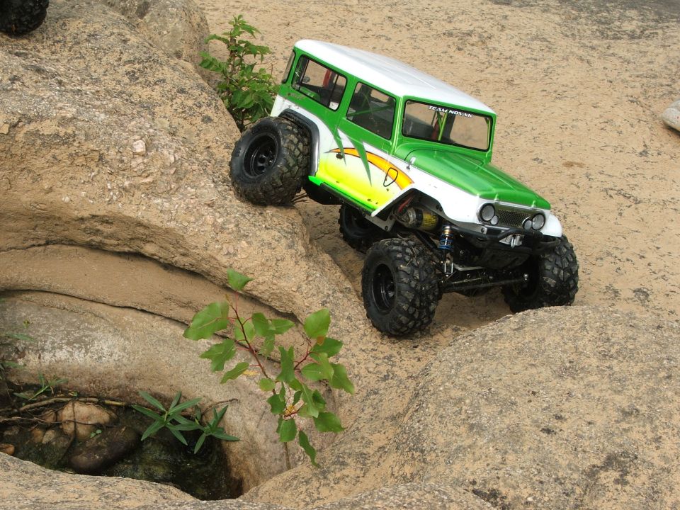 Green and white RC rock crawler climbing over rocks