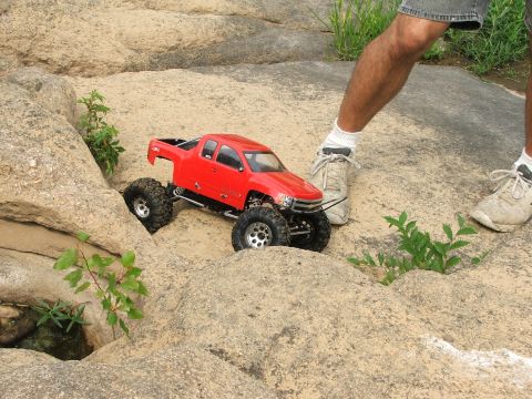 1996 Ford Bronco - RC rock crawler truck navigating a rocky obstacle course with a person nearby.