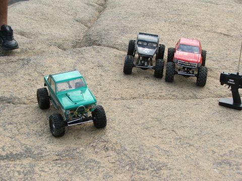 1996 Ford Bronco - Three remote control rock crawling trucks are positioned on a rocky surface, with a remote control in the foreground.