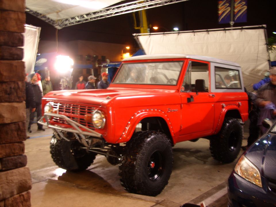 Lifted red Ford Bronco with white top, tube bumper and big off-road tires at a night event