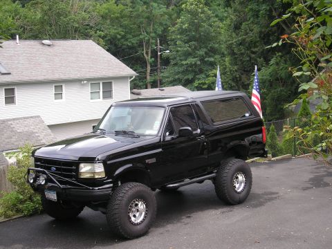 1995 Ford Bronco - A lifted black Ford Bronco is parked in a residential driveway with American flags in the background.