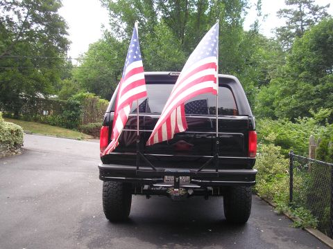 1995 Ford Bronco - Rear view of a black SUV with American flags attached to a rack.