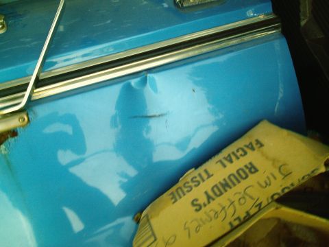 2001 Dodge 2500 - A close-up view of a dented blue vehicle door, with a box of tissues resting on it.