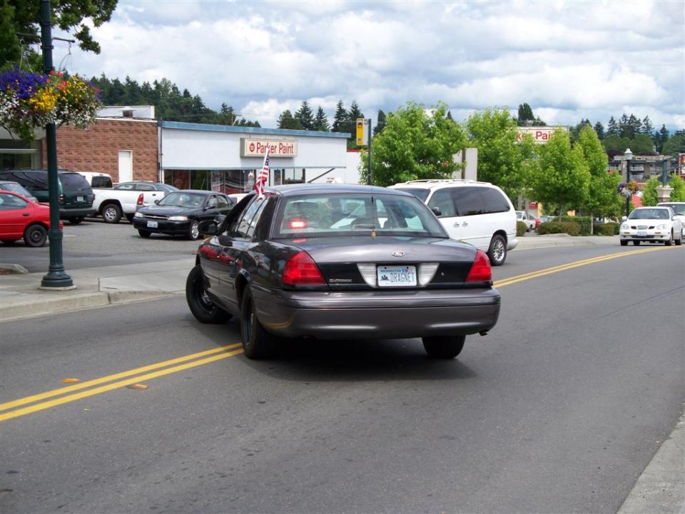 Gray Ford Crown Victoria with DRAGNET Washington plate and American flag driving through a small town