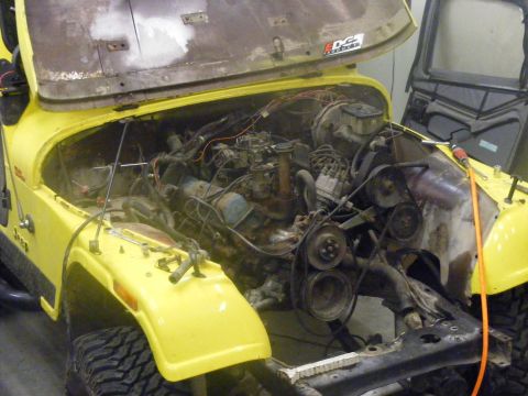 1981 Jeep CJ7 - Yellow Jeep CJ in a garage mid-teardown with the hood propped up, grille and radiator support removed, and the passenger-side inner fender…