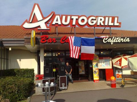 1991 Ford Crown Victoria - The entrance to an Autogrill restaurant features American and French flags, a man, and sound equipment set up outside.
