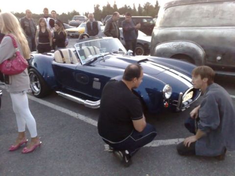 1991 Ford Crown Victoria - A group of people gather around a classic blue convertible sports car at an outdoor car meet.