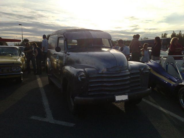 Panel van truck with a wide grille, parked next to a yellow car and a blue buggy