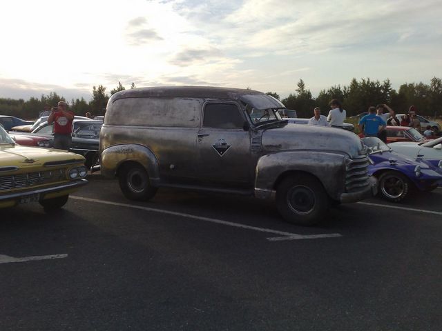 Vintage panel van with a diamond emblem on the door, parked at an outdoor car meet. Other cars are visible